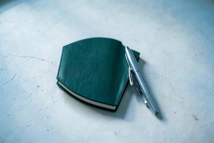 Pequeno caderno de anotações com uma caneta ao lado, em cima de uma mesa