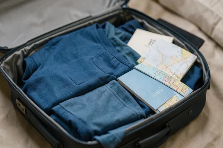 Uma mala de viagem aberta com roupas dobradas e alguns itens essenciais organizados, como um guia de viagem e um mapa.