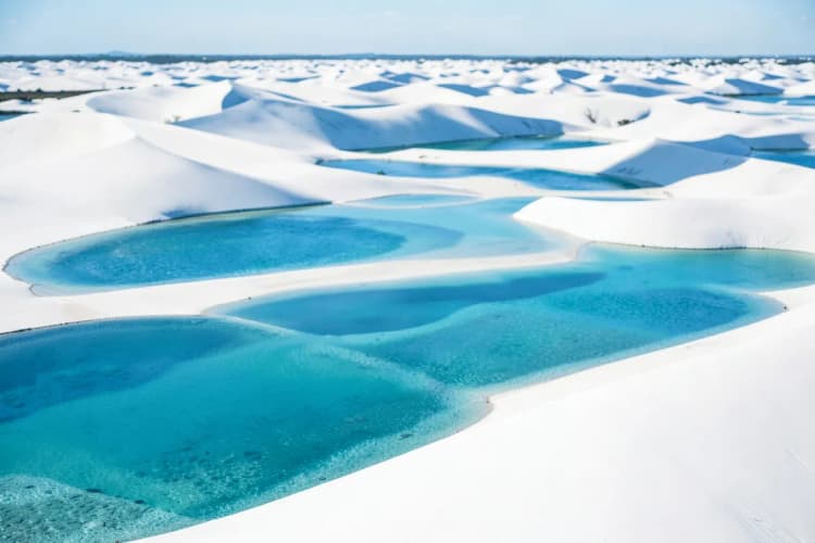 Extensas dunas de areia branca com lagoas de água cristalina nos Lençóis Maranhenses